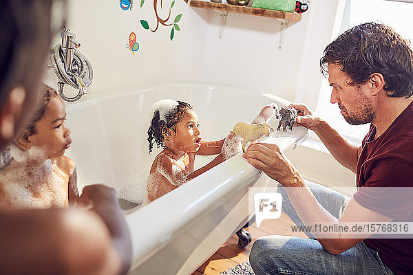 Vater und Tochter spielen in der Badewanne mit Spielzeugtieren