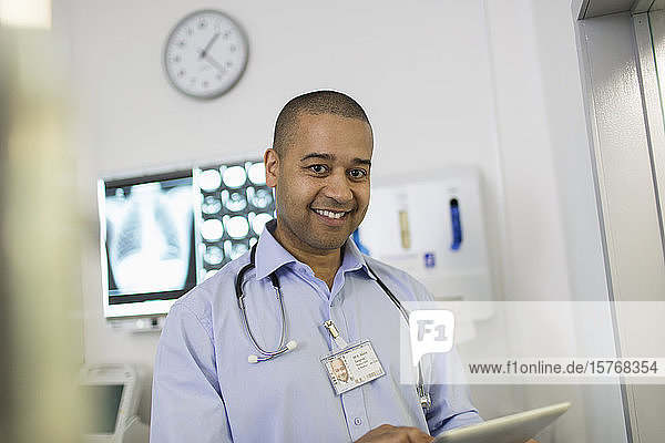 Porträt eines selbstbewussten  lächelnden männlichen Arztes  der ein digitales Tablet im Krankenhaus benutzt