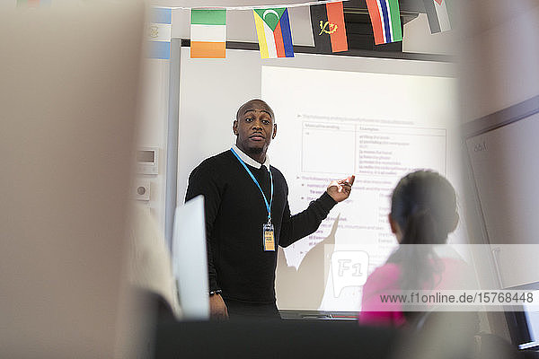 Männlicher Community-College-Lehrer  der eine Unterrichtsstunde an der Projektionsfläche im Klassenzimmer leitet