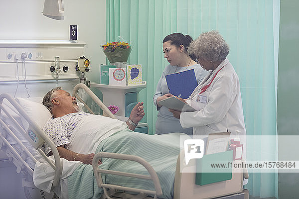 Ärzte mit Krankenblatt machen Visite  sprechen mit älterem Patienten im Krankenhauszimmer