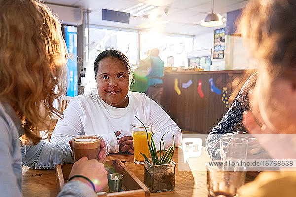 Lächelnde junge Frau mit Down-Syndrom im Gespräch mit Freunden in einem Café
