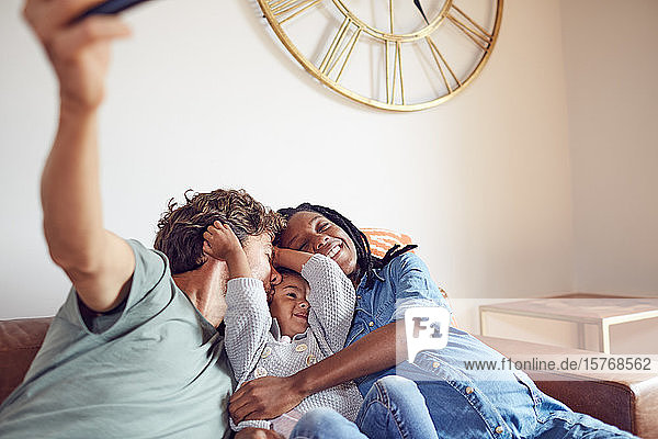 Liebevolle junge schwangere Familie  die ein Selfie auf dem Wohnzimmersofa macht