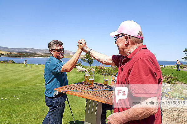 Glückliche männliche Golffreunde  die sich die Hände reichen und Bier trinken