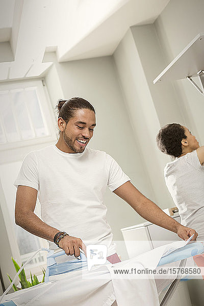 Junger Mann macht Wäsche  bügelt Hemd in Waschküche