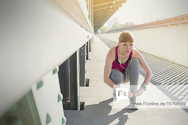 Fokussierte junge Läuferin beim Schuhbinden auf einem sonnigen Bahnsteig