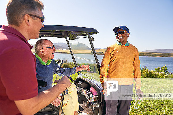 Männliche Golffreunde unterhalten sich und lachen am Golfwagen