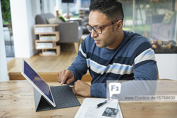 Konzentrierter Mann beim Bezahlen von Rechnungen am digitalen Tablet