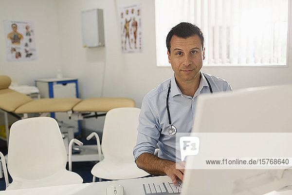 Portrait confident male doctor working at computer in doctors office