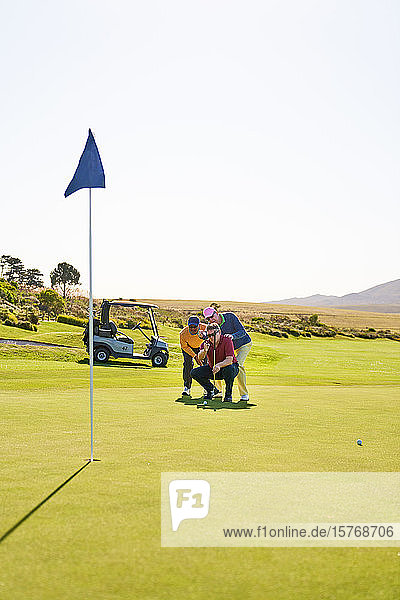 Männliche Golfer planen einen Putt auf dem sonnigen Putting Green eines Golfplatzes