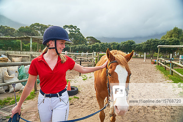 Teenager-Mädchen mit Reithelm führt Pferd auf der Koppel