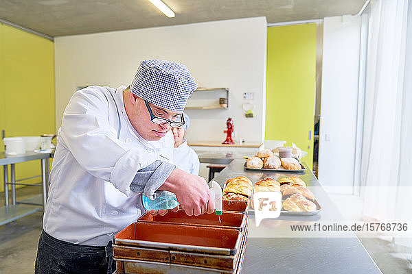 Konzentrierter junger Mann mit Down-Syndrom backt Brot in der Küche