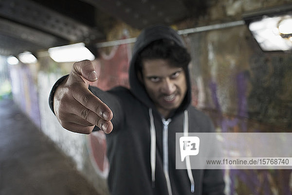 Porträt eines bedrohlich wirkenden jungen Mannes  der in einem städtischen Tunnel mit dem Finger eine Pistole zeigt