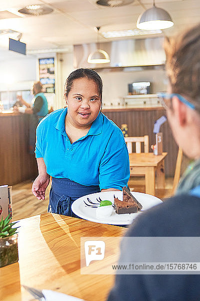 Junge Kellnerin mit Down-Syndrom serviert Dessert in einem Cafe