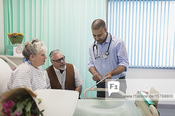 Arzt mit digitalem Tablet bei der Visite  Gespräch mit älterem Ehepaar im Krankenhauszimmer