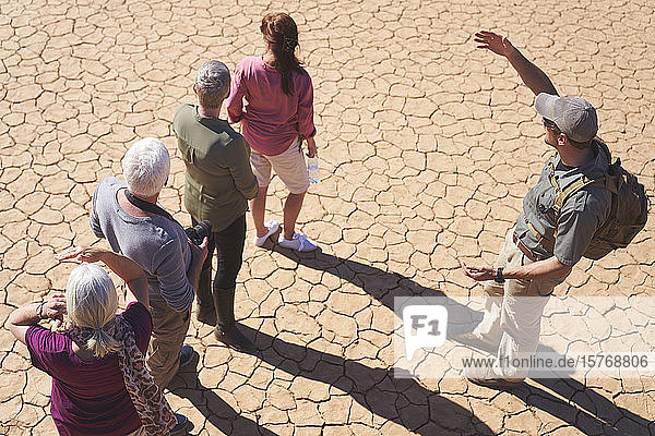 Safari tour guide talking with group on sunny cracked earth