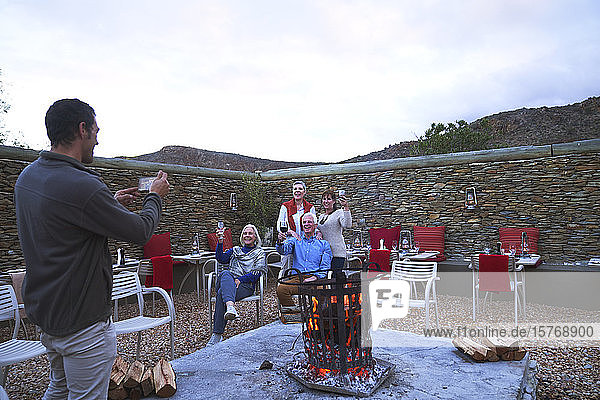 Ältere Freunde mit Wein posieren für ein Foto an der Feuerstelle auf der Terrasse