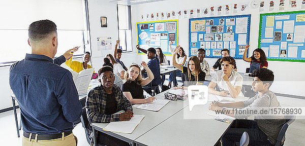 High school teacher calling on students with hands raised in classroom