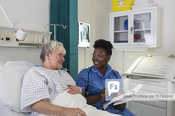 Weibliche Krankenschwester im Gespräch mit einem älteren Patienten im Krankenhauszimmer