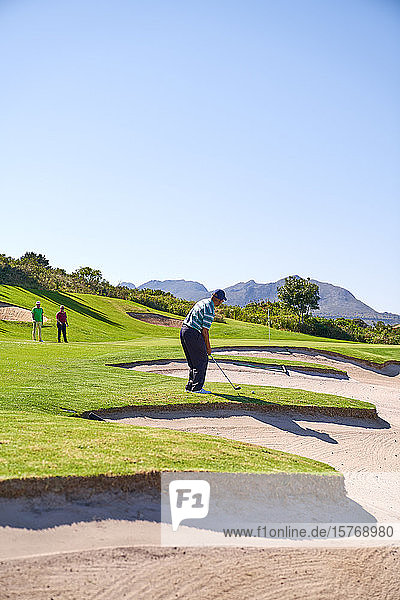 Männlicher Golfer bereitet sich auf einen Schlag über einem sonnigen Golfplatzbunker vor