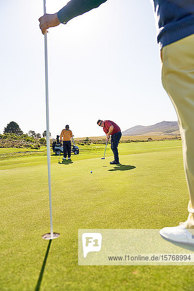 Männlicher Golfer  der auf einem sonnigen Golfplatz auf den Stift und das Loch zielt