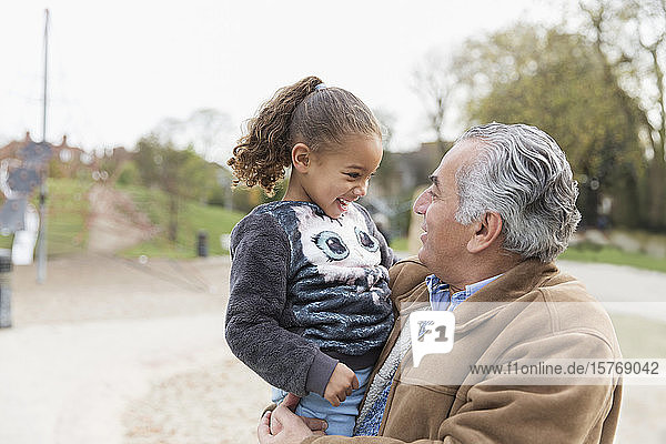 Smiling grandfather holding granddaughter at park