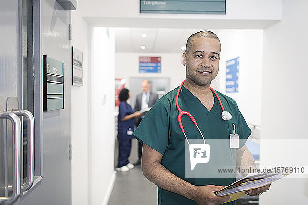 Portrait confident male doctor with medical chart making rounds in hospital corridor