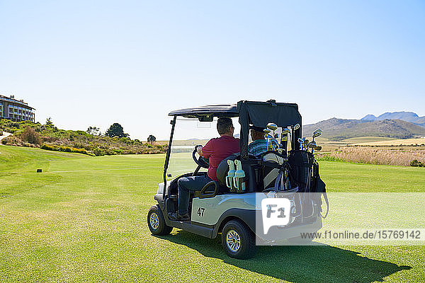 Männliche Golfer fahren Golfwagen auf sonnigen Golfplatzgrüns