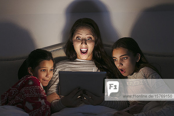 Überrascht Mutter und Töchter beobachten Film auf digitalen Tablet in dunklen Schlafzimmer