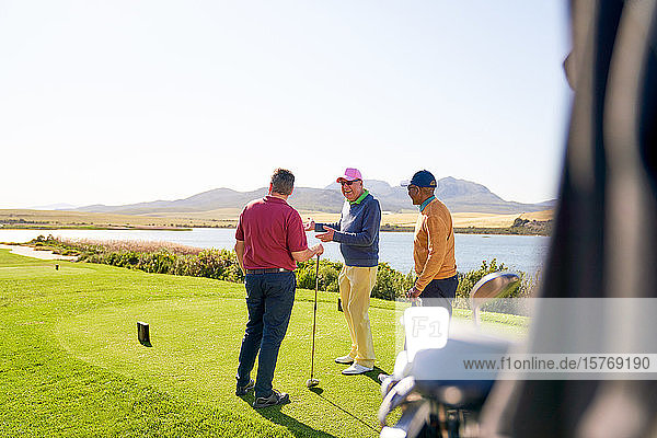 Männliche Golfer unterhalten sich am Abschlagplatz auf einem sonnigen Golfplatz