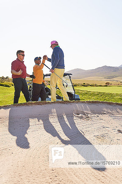 Männliche Golfer beim Feiern hinter dem sonnigen Golfbunker