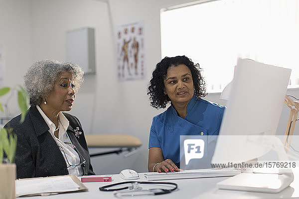 Female doctor meeting with senior patient at computer in doctors office
