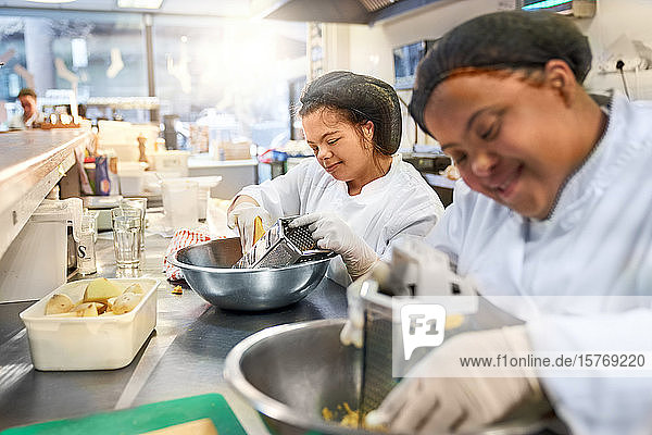 Smiling young women with Down Syndrome grating cheese in cafe kitchen