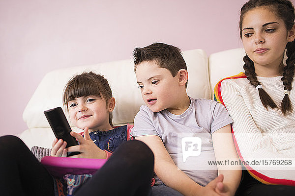 Schwestern und Bruder mit Down-Syndrom sehen auf dem Sofa fern