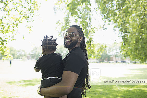 Porträt glücklicher Vater mit langen Zöpfen  der sein Kleinkind im Park hält