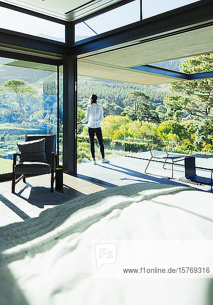 Frau steht auf sonniger  luxuriöser Terrasse mit Blick auf Bäume