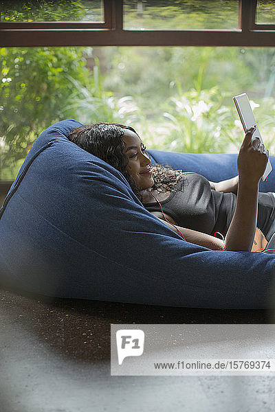 Glückliche junge Frau entspannt sich mit digitalem Tablet in Sitzsackstuhl