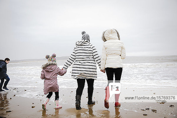 Familie in warmer Kleidung beim Spaziergang am winterlichen Meeresstrand