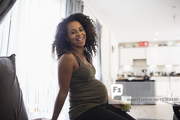 Portrait glückliche junge schwangere Frau trinkt grünen Smoothie