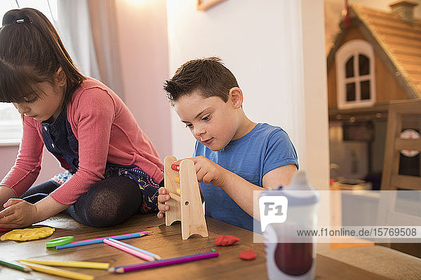 Konzentrierter Junge mit Down-Syndrom spielt mit Spielzeug am Tisch