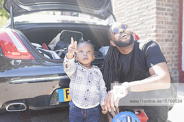 Vater und neugieriges Kleinkind schauen hinter dem Auto hervor