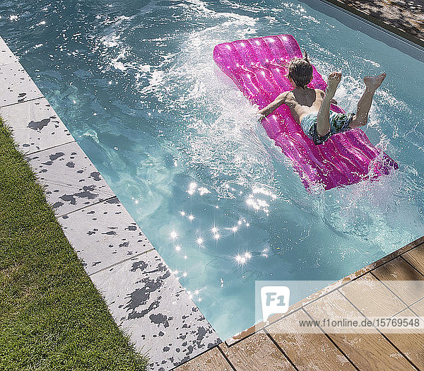 Playful boy jumping on inflatable raft in sunny summer swimming pool