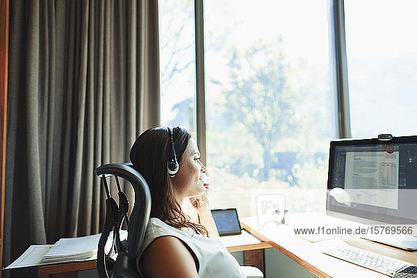 Geschäftsfrau mit Headset bei der Arbeit am Computer im sonnigen Heimbüro