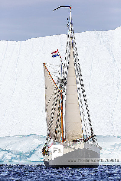 Schiff mit niederländischer Flagge  das auf dem Atlantik an einem Eisberg vorbeifährt Grönland