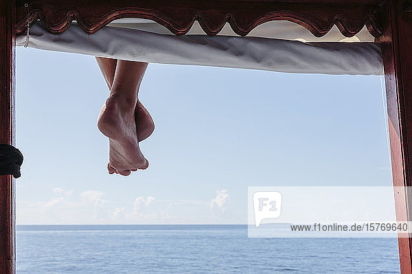 Nackte Füße hängen vom Steg über dem sonnigen Ozean  Malediven