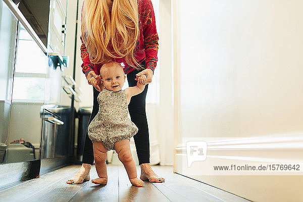 Porträt Mutter hilft Baby Tochter gehen im Korridor