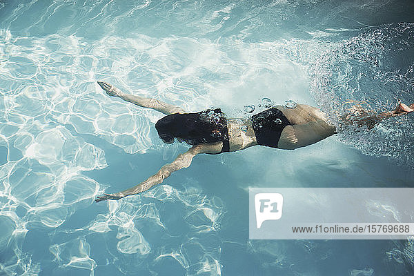 Frau im Bikini schwimmt unter Wasser im sonnigen Schwimmbad