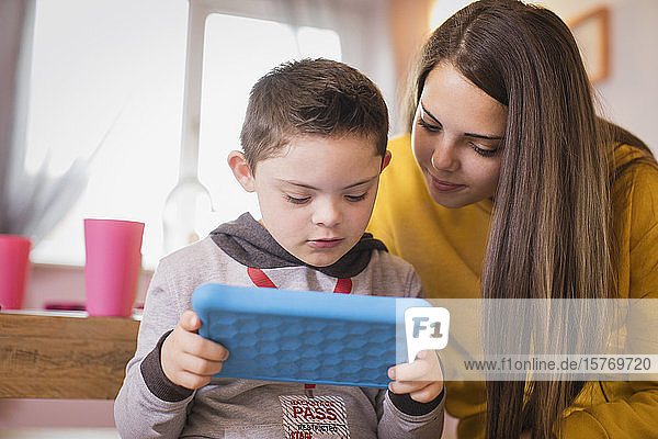 Girl watching brother with Down Syndrome using digital tablet