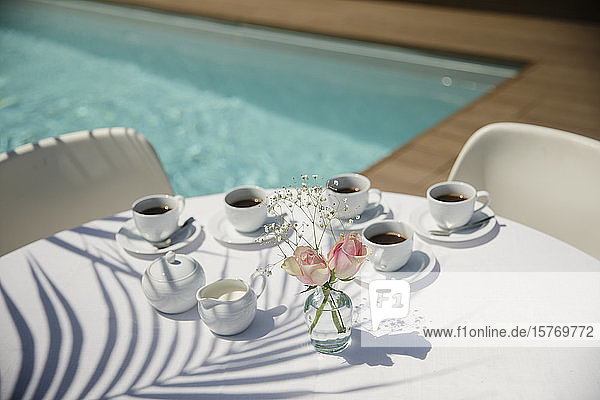 Coffee cups and roses on sunny summer poolside patio table