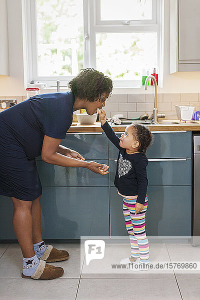 Cute daughter feeding pregnant mother in kitchen