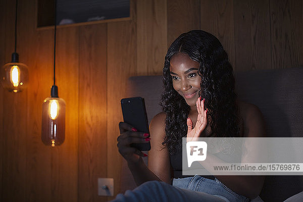 Glückliche junge Frau  die mit ihrem Smartphone auf dem Bett einen Videochat führt
